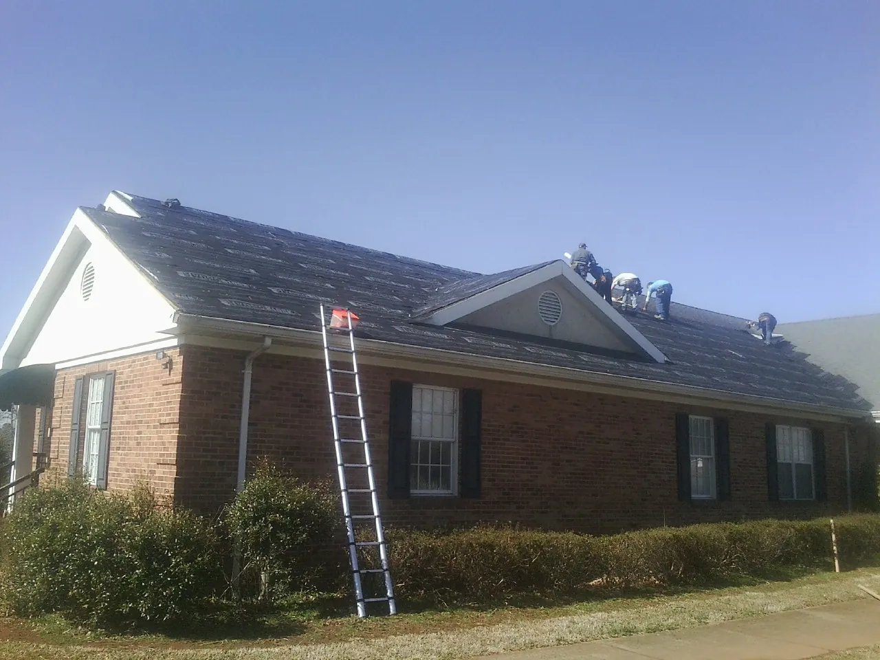 Crew tearing shingles off a brick ranch roof with a ladder set — Metal Roof Repair work by our crew in Kaufman