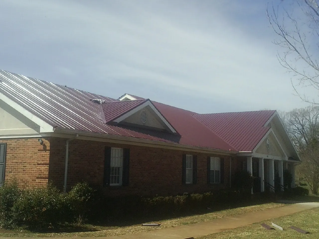 Red metal roof with gabled entries on a long brick building, from a Hail Damage Roof Repair job in Kaufman