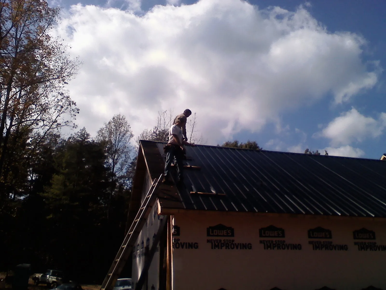 Roofer fastening dark metal panels high against a cloudy sky, from a Roof Inspection job in Kaufman