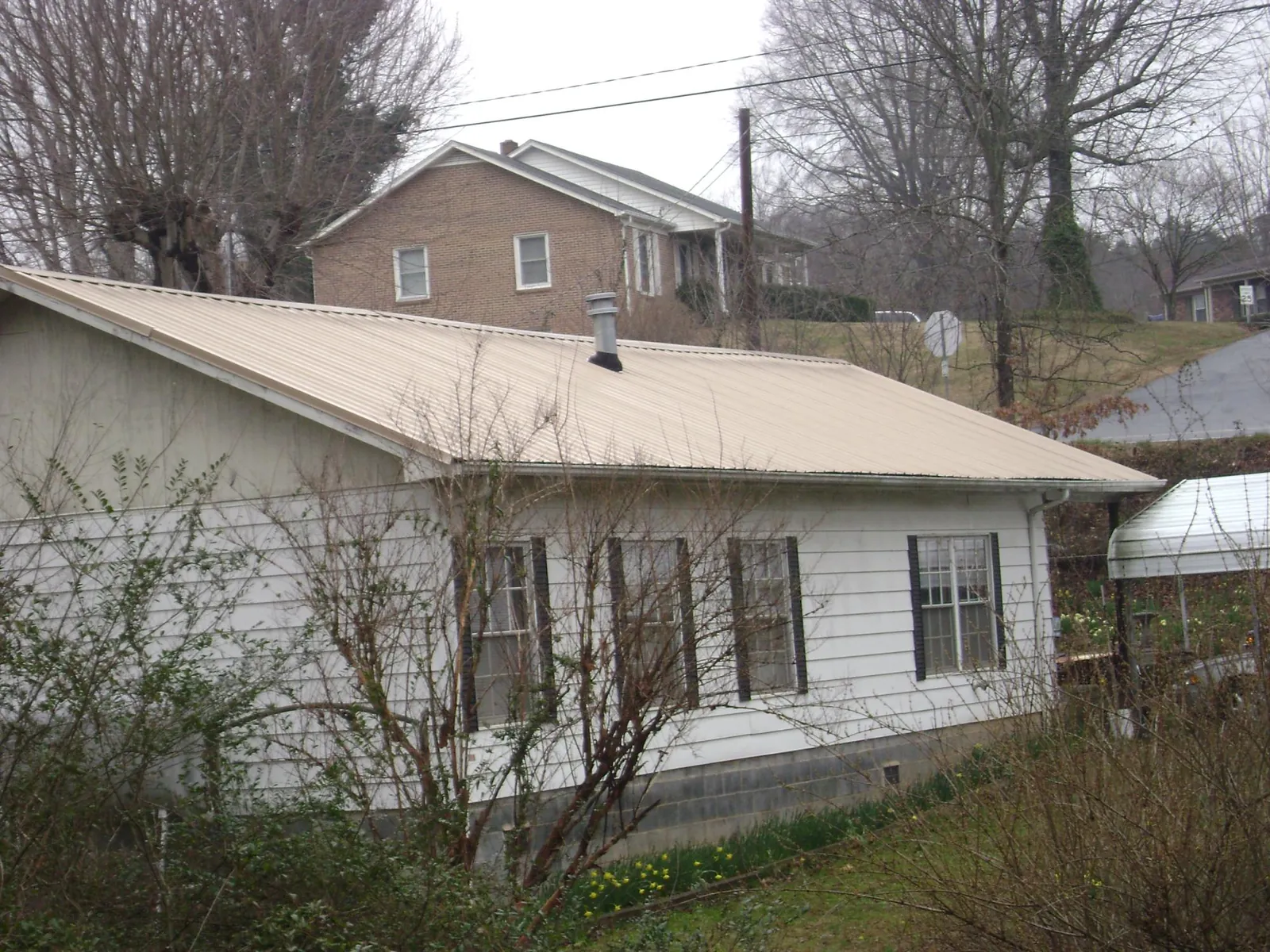 Tan metal roof on a white sided house set into a hillside — Commercial Roofing by Roofing Brothers in Kaufman